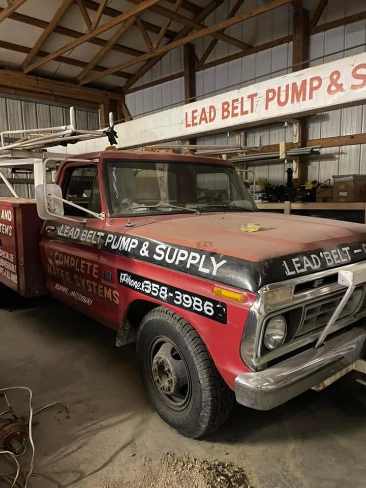 An old red Lead Belt Pump & Supply service truck parked inside the shop, hand lettered with Complete Water Systems, Elvins, Missouri
